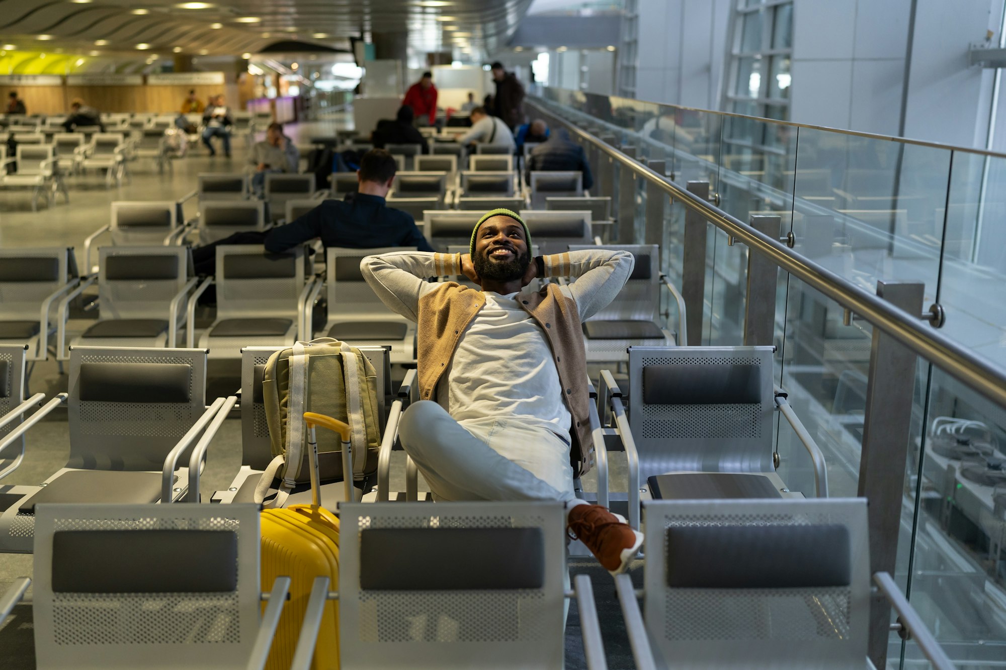 Happy black man sitting in airport resting, waiting landing on board looking up, dreams of travel.